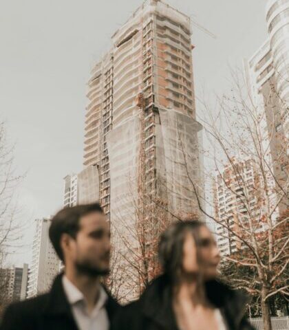 A couple stands in front of a high-rise construction site, blending urban development with human presence.