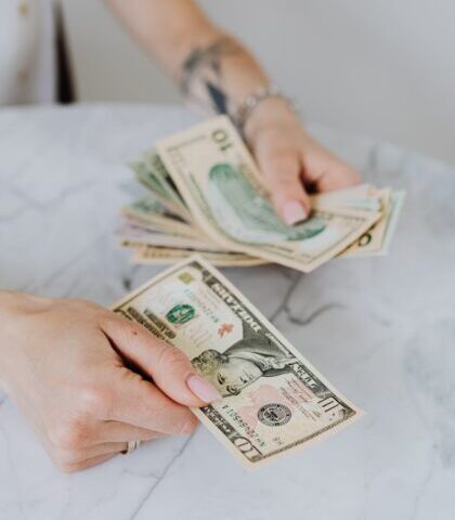 Close-up of hands counting US dollar bills on a marble table, symbolizing personal finance.