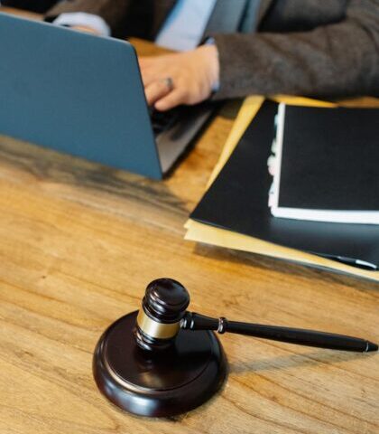 From above of crop anonymous male lawyer in formal clothes typing on laptop while sitting at wooden table with stack of documents and gavel